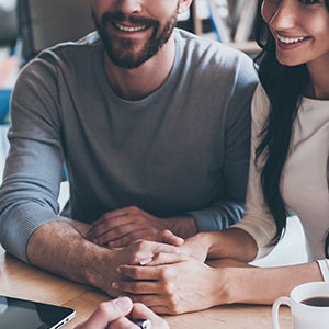 Feeling so happy now. Close-up of happy young loving couple hold Feeling so happy now. Close-up of happy young loving couple holding hands and looking at man sitting in front of them at the desk